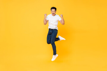 Fototapeta na wymiar Happy energetic young Asian man jumping yelling and clenching fists isolated on yellow studio background