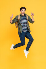 Fototapeta na wymiar Happy smiling young Asian tourist man with backpack jumping and giving thumbs up isolated on yellow background