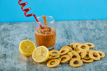 A glass of juice with straw, lemons and crackers on gray table