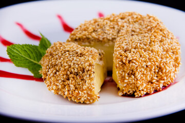 Deep-fried brie cheese with sesame seeds garnished with fresh mint leaf and lingonberry sauce