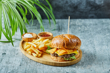 Big burger with fry potato in the wooden plate on the marble background