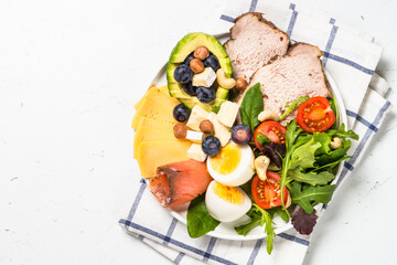 Keto diet plate. Low carb dish, healthy nutrition. Baked meat, eggs, avocado, salad leaves, cheese and fish. Top view.