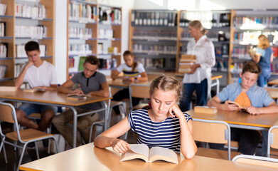 Schoolgirl preparing for lesson in school library, reading textbooks