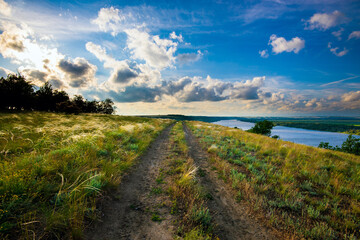 Dirt road in the steppe between feather fields grass and parallel with river