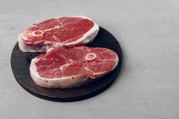 Raw rib-eye beef steak on wooden cutting board on gray background