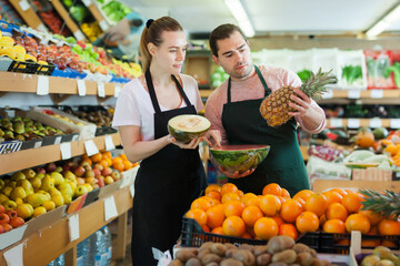 Obraz premium Happy saleswoman and salesman holding half of watermelon in hands in fruit store