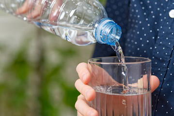 boy is pouring water from the plastic bottle into the glass on wooden table