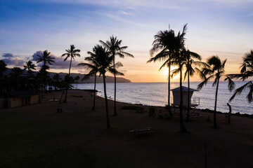 Obraz premium Little lifeguard cottage between palm trees on a Caribbean beach on Hawaii with a colorful view of the calm sea at sundown