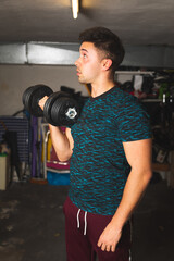 Young caucasian man raising weights at the garage