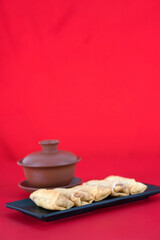 A plate of fried spring rolls and a bowl of tea on a red background