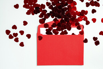 Small red heart-shaped confetti in a red envelope on a white background top view