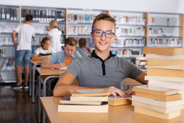 Schoolboy sitting with stacks of books in school library indoor