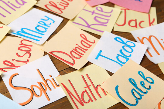 Paper notes with different baby names on wooden table