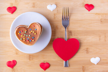 Homemade heart shaped pancakes with sugar decoration on a white plate, a fork and a red heart shape...
