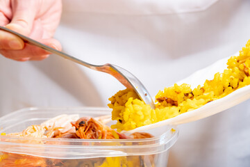 Closeup of a hand transferring the Spanish seafood rice with prawns and crayfish to the container