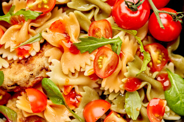 Color Farfalle ready-made pasta with chicken cutlets with herbs and tomatoes. A variety of types and forms of Italian pasta. pasta in the form of bows in a round plate on a gray background, top view