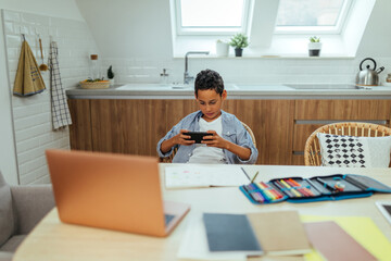 Afro boy sitting at the desk and playing game via phone