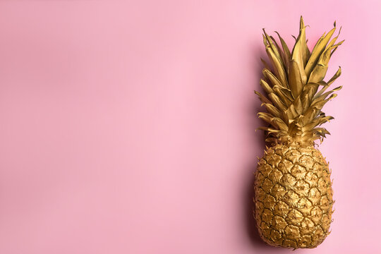 Top view of painted golden pineapple on pink background, space for text. Creative concept