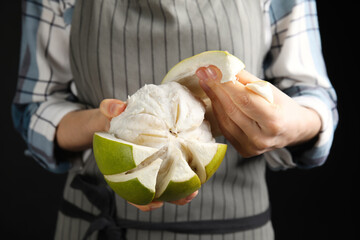 Woman peeling fresh ripe pomelo on black background, closeup