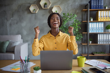 Photo of happy afro american business woman raise fists win sit workplace laptop desk lucky deal...