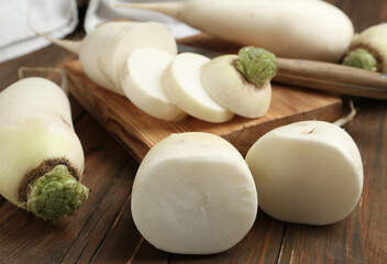 Cut and whole white turnips on wooden table, closeup