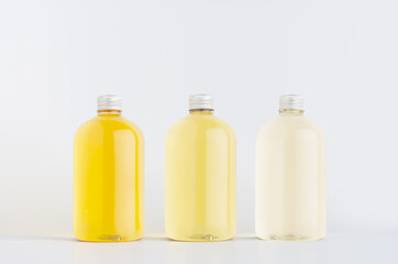 Assortment of three plastic low thick bottles with pale fresh drink different yellow colors or cosmetic essential oil, silver cap mockup on white background, template.