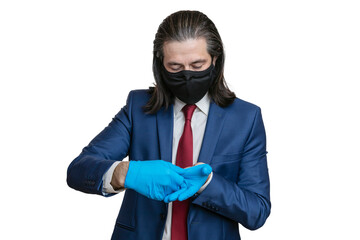 A young man in a business suit, in a protective mask, takes off medical gloves from his hands on a white background. The manager takes off his gloves after a working day.