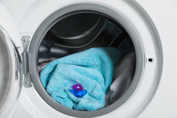 Laundry detergent capsule and towels in washing machine drum, closeup view
