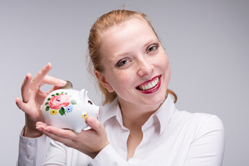 Fototapeta na wymiar happy red-haired woman putting a coin into her porcelain bank
