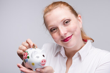 Fototapeta na wymiar happy red-haired woman putting a coin into her piggy bank