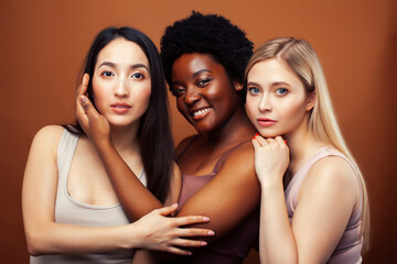 Obraz premium young pretty asian, caucasian, afro woman posing cheerful together on brown background, lifestyle diverse nationality people concept