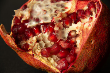 the ripe fruit of the red pomegranate is half peeled and lies on a dark background