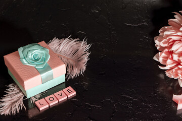 Beautiful pink composition and a black background. Dahlia flower, present box and word love made of wooden letters
