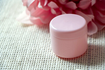 Pink cosmetic jar on a sackcloth background. Pink dahlia flower in a corner