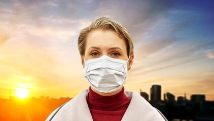 health, safety and pandemic concept - young woman wearing protective medical mask over sunset in city on background