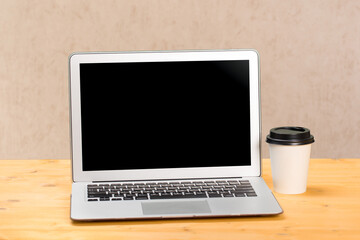 Mockup blank laptop screen with coffee on wooden table in coworking space.