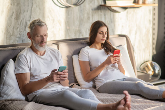 Man and woman with smartphones sitting on bed