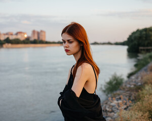 Red-haired Woman in a black dress near the river in nature
