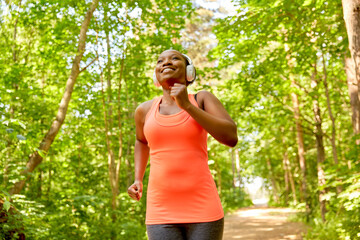 fitness, sport and healthy lifestyle concept - happy smiling young african american woman in headphones running in park