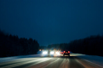 Fototapeta na wymiar Night highway in winter. Light headlights in the dark, the movement of cars from the viewer