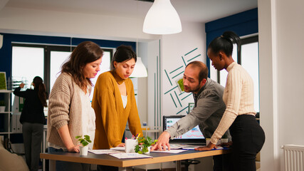 Diverse business people communicating in start up business office standing over desk looking through financial documents. Multiethnic team analysing company informations in modern workplace