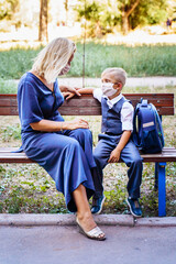 Mom and her son, a schoolboy, are sitting on a bench in the yard. They put on medical masks to protect themselves from the coronavirus. Important methods of protection against Covid-19