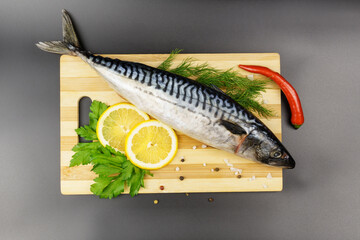 Raw mackerel on a wooden cutting board with spices, herbs and lemon on a black background.