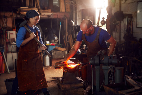 Male And Female Blacksmiths Hammering Metalwork On Anvil With Sparks