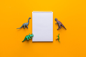 notepad or copybook and toys dinosaurs on a yellow background. minimalistic set composition. kids...