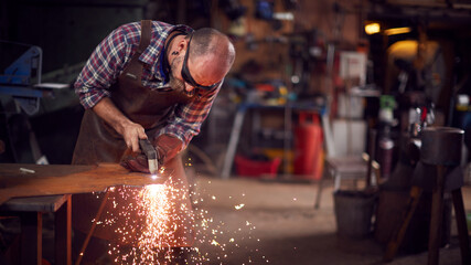 Male Blacksmith Using Plasma Cutter To Cut Shape From Sheet Metal In Forge