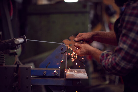 Close Up Of Male Blacksmith Shaping Metalwork On Belt Sander With Sparks