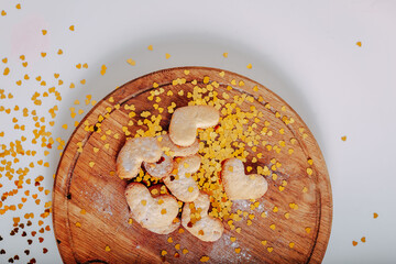 Heart-shaped cookies on round wooden cutting board. Saint Valentine's cookies in shape of heart and golden sparkles on white background. Golden glitters in shape of heart on white background.