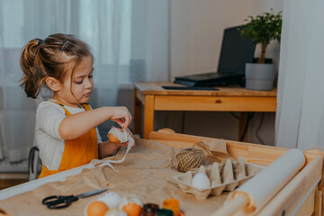 Baby girl decorating easter eggs on white table. Kid decorating eggs with kraft paper, lace and...