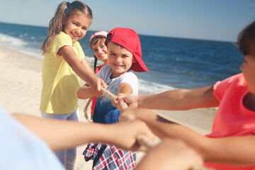 Cute children pulling rope during tug of war game on beach. Summer camp